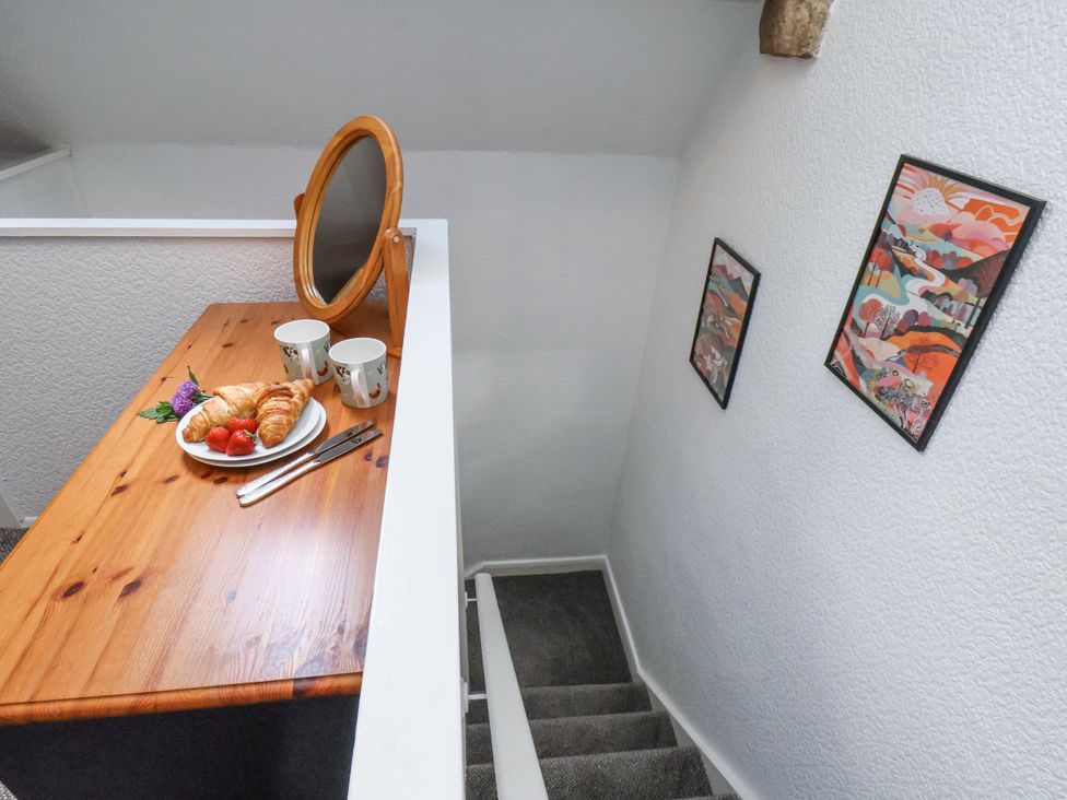 A wooden desk with a round mirror mugs croissants strawberries and cutlery next to a staircase with colorful framed pictures on the wall at Wayside Farm Dairy Cottage Cloughton near Burniston