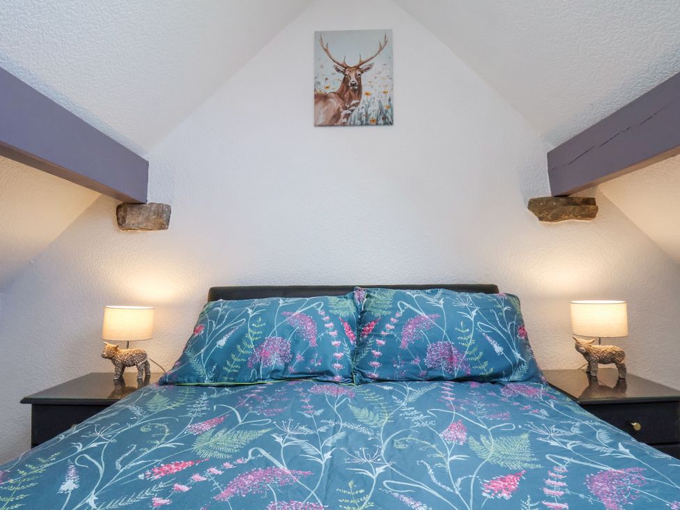 A bedroom with a bed with floral bedding two bedside tables with lamps and small animal figurines and a deer painting on the wall at Wayside Farm Dairy Cottage in Cloughton near Burniston