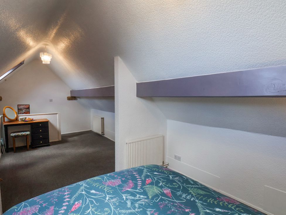 An attic bedroom with a bed, a dressing table with a mirror and stool, radiators and a sloped ceiling at Wayside Farm Dairy Cottage in Cloughton near Burniston
