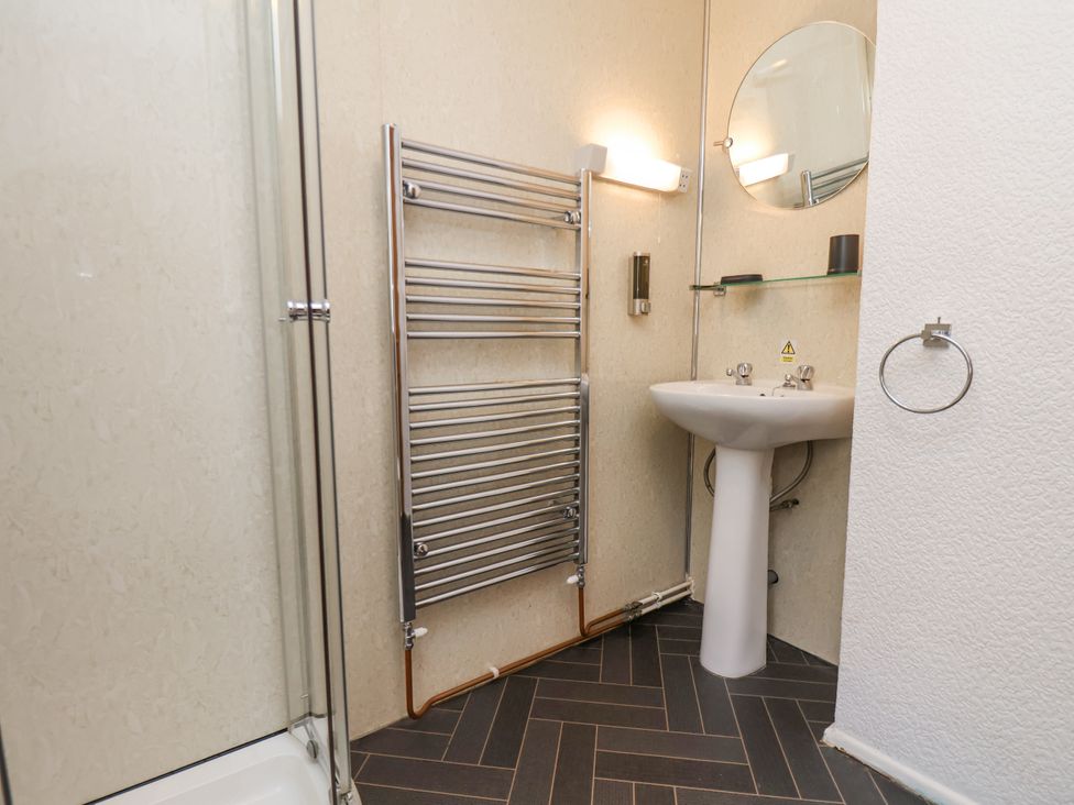 A bathroom with a shower, towel rack, pedestal sink, mirror, and soap dispenser at Wayside Farm Dairy Cottage in Cloughton near Burniston