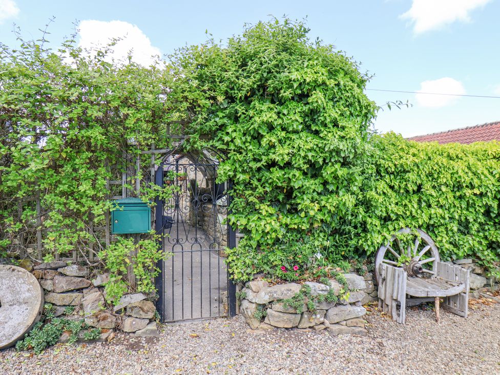 An outdoor iron gate surrounded by greenery with a mailbox on the left and a wooden bench made from a wagon wheel on the right at Wayside Farm Dairy Cottage in Cloughton near Burniston