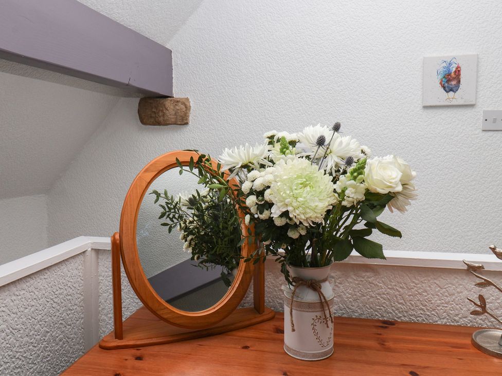A mirror and a vase of flowers on a table at Wayside Farm Dairy Cottage, Cloughton near Burniston