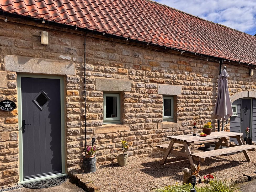 A patio area with a table and umbrella at Wayside Farm Dairy Cottage Cloughton near Burniston