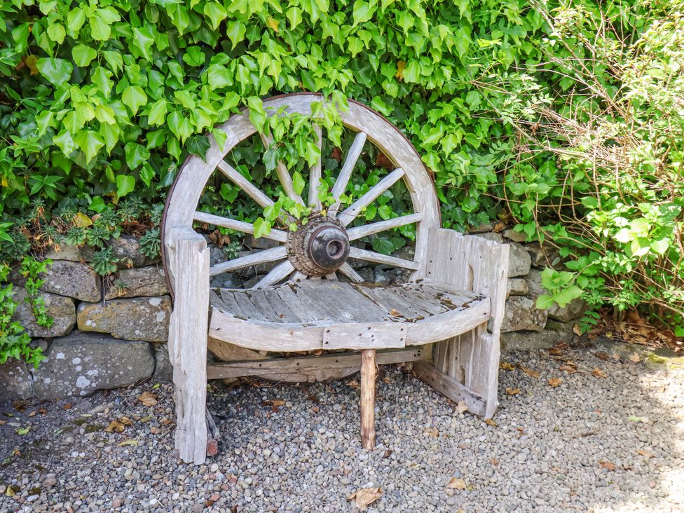 A wooden bench with a wagon wheel backrest in a garden with ivy and stone wall behind at Wayside Farm Stable Cottage Cloughton near Burniston