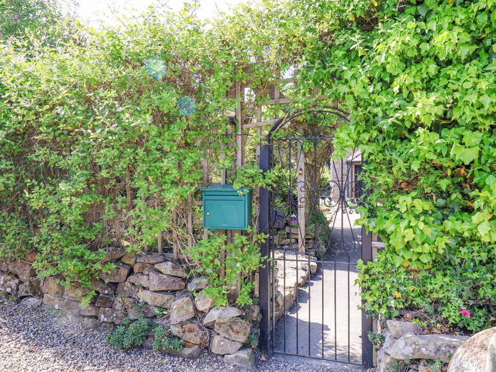 An iron garden gate surrounded by green foliage and stone wall with a green mailbox at Wayside Farm Stable Cottage in Cloughton near Burniston