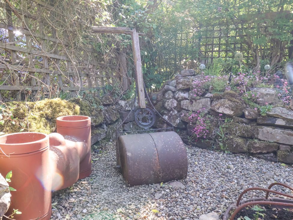 A garden area with gravel ground a metal roller two clay pipes and stone walls with plants at Wayside Farm Stable Cottage in Cloughton near Burniston