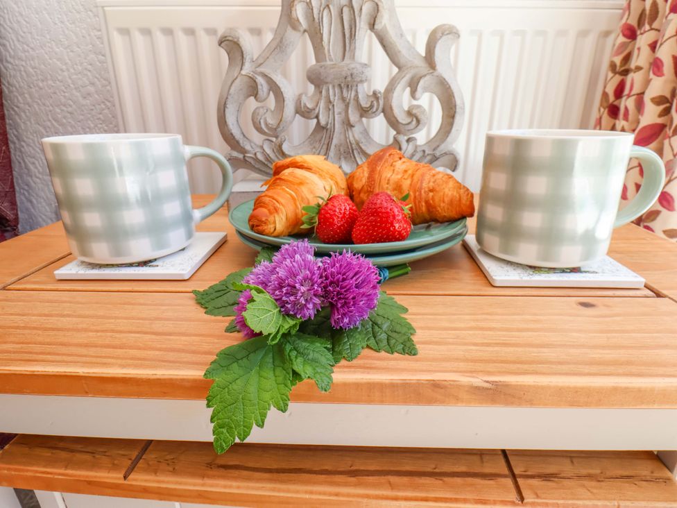 A kitchen table with coffee mugs, croissants, strawberries, and a decorative flower at Wayside Farm Stable Cottage Cloughton near Burniston