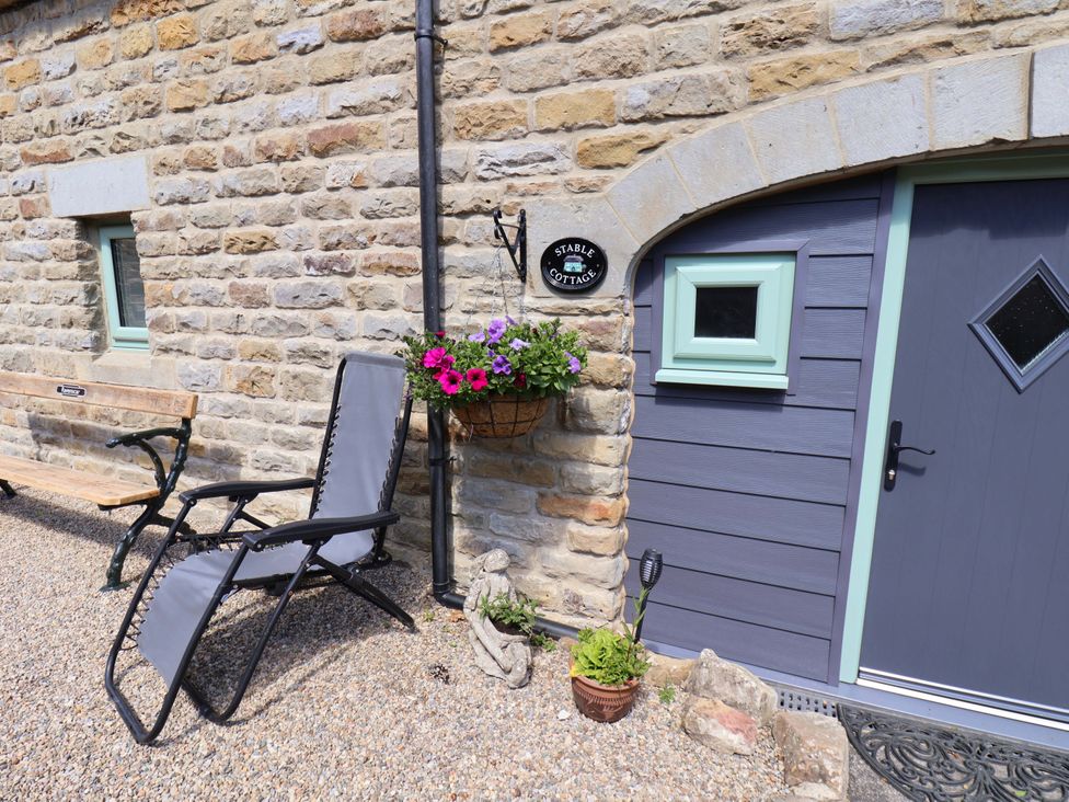 An outdoor seating area with a bench and lounge chair at Wayside Farm Stable Cottage in Cloughton near Burniston