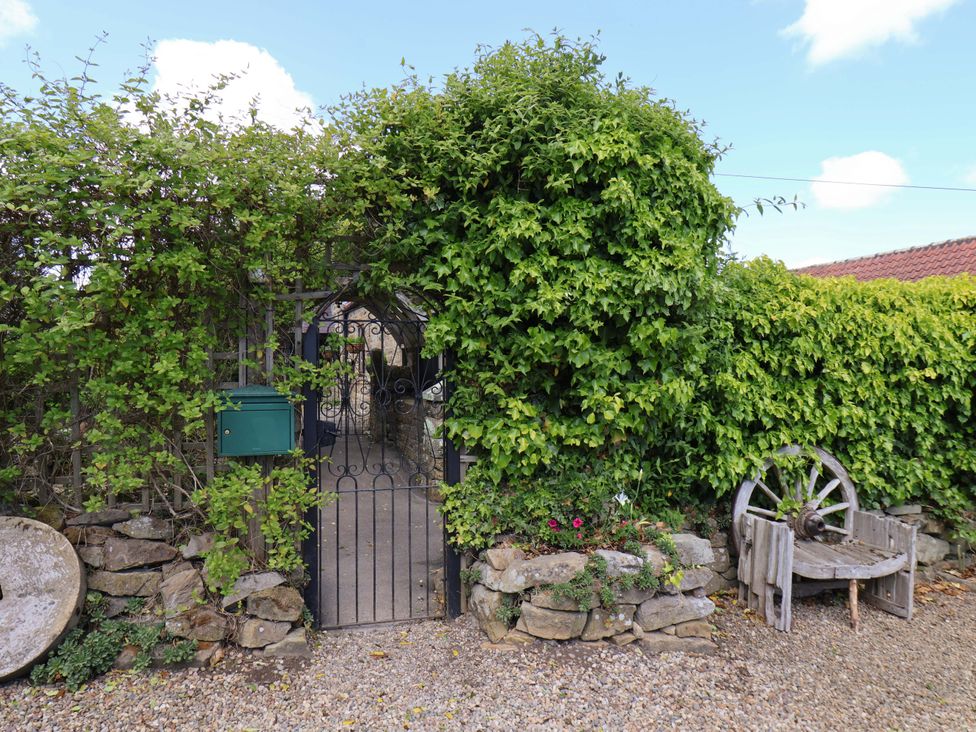 An entrance gate with a stone wall and plants at Wayside Farm Stable Cottage in Cloughton near Burniston