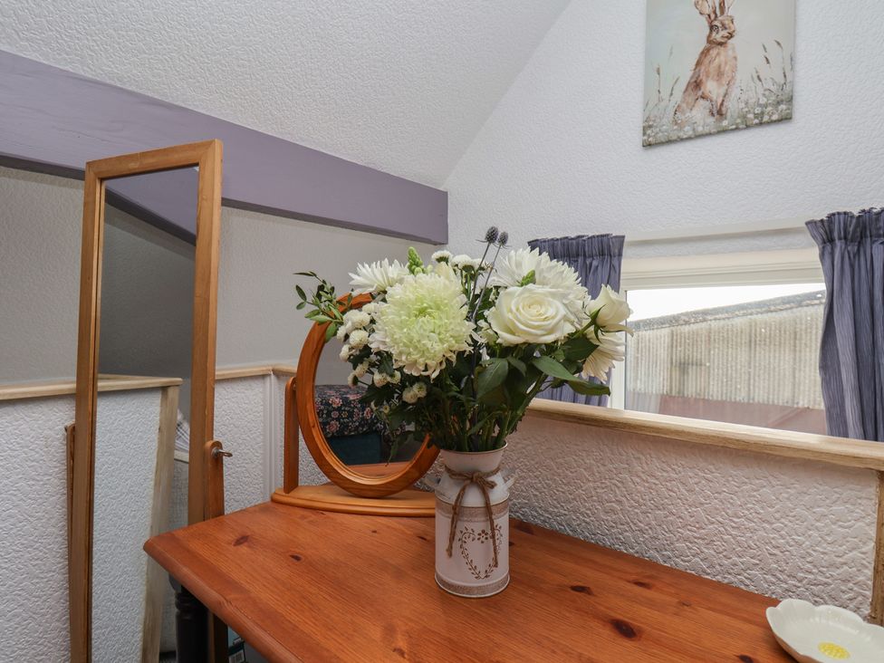 A bedroom with a table, flowers in a vase, and a mirror at Wayside Farm Stable Cottage, Cloughton near Burniston