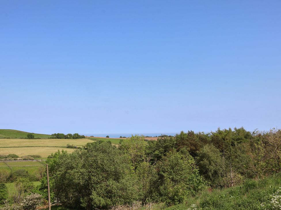 A view of fields and trees with the sea in the distance at Wayside Farm Cart Cottage Cloughton near Burniston