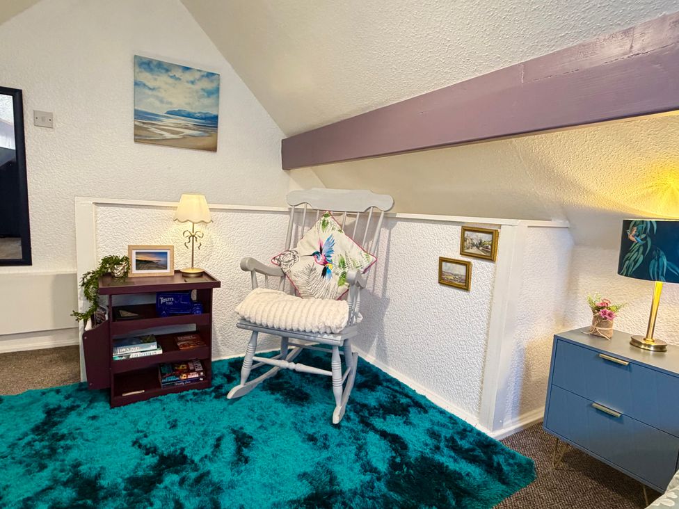 A snug area with a rocking chair and bookshelf at Wayside Farm Cart Cottage Cloughton near Burniston