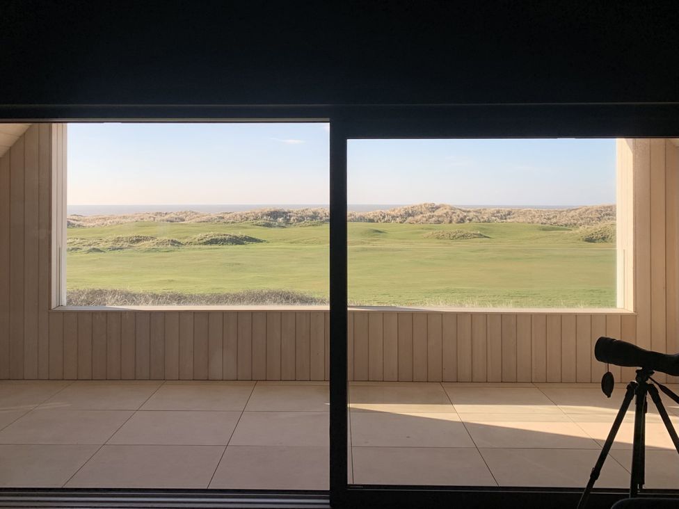 A view of grass and dunes through a large window at Twyn Isaf in Borth