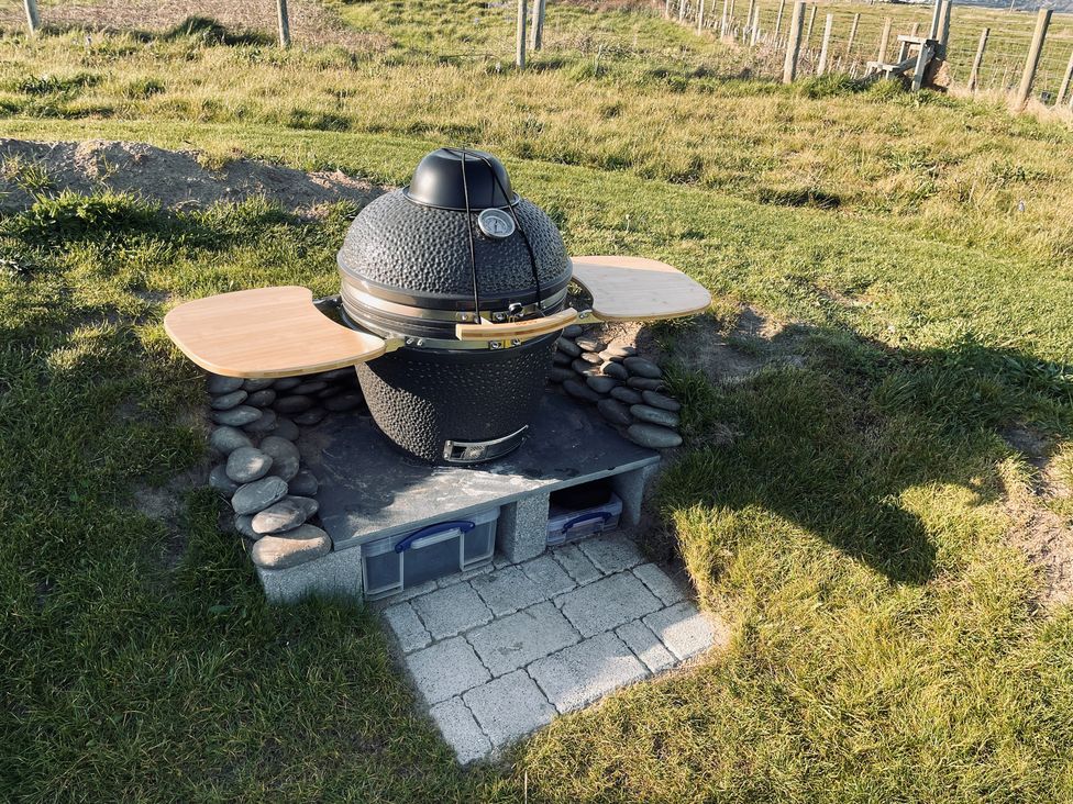 A barbecue grill on a stone base with a wooden table at Twyn Isaf in Borth