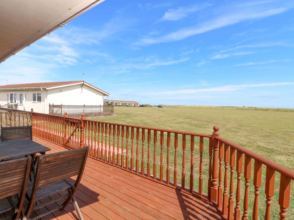 A deck with a table and chairs overlooking a grassy area at Boa Vista in Bacton