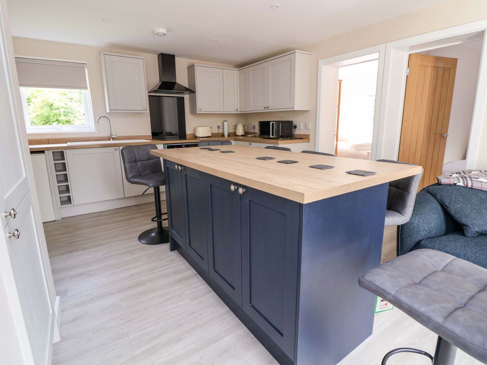 A kitchen with an island and stools at Cartref in Pen Y Ball near Holywell