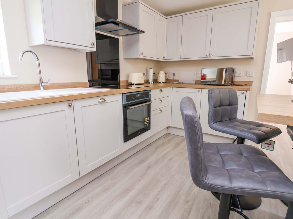 A kitchen with bar stools and appliances at Cartref in Pen Y Ball near Holywell