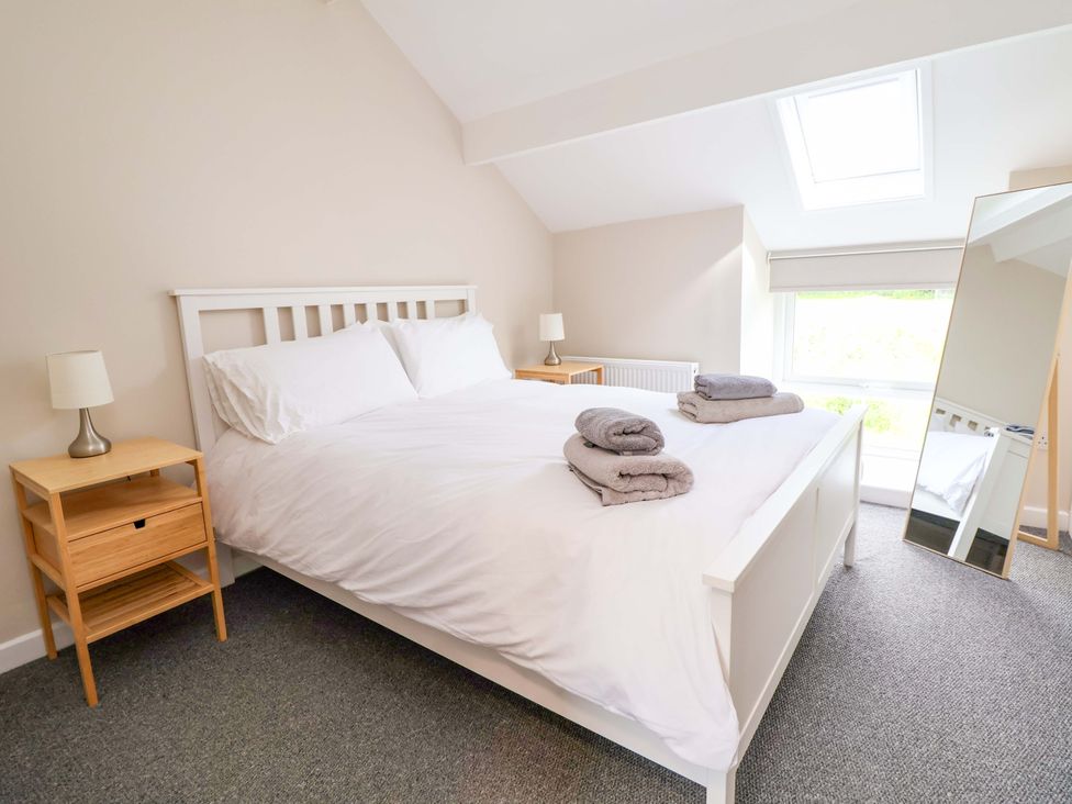 A bedroom with a bed, side table, lamp, and mirror at Cartref Pen Y Ball near Holywell