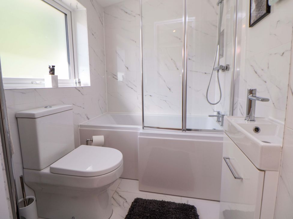 A bathroom with a bathtub, toilet, sink and window at Cartref Pen Y Ball near Holywell