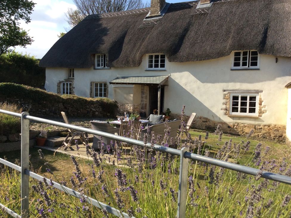 An outdoor area with a thatched roof house and a table with chairs at Westacombe Farm Dunsford near Tedburn St Mary