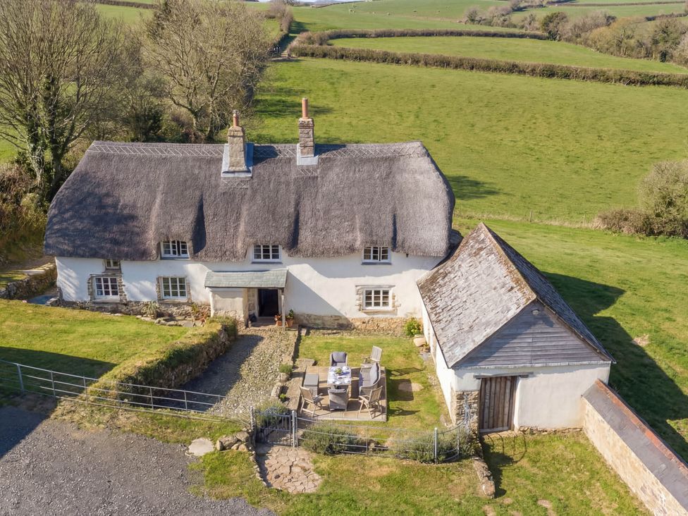 A house with a thatched roof and outdoor seating at Westacombe Farmhouse in Dunsford