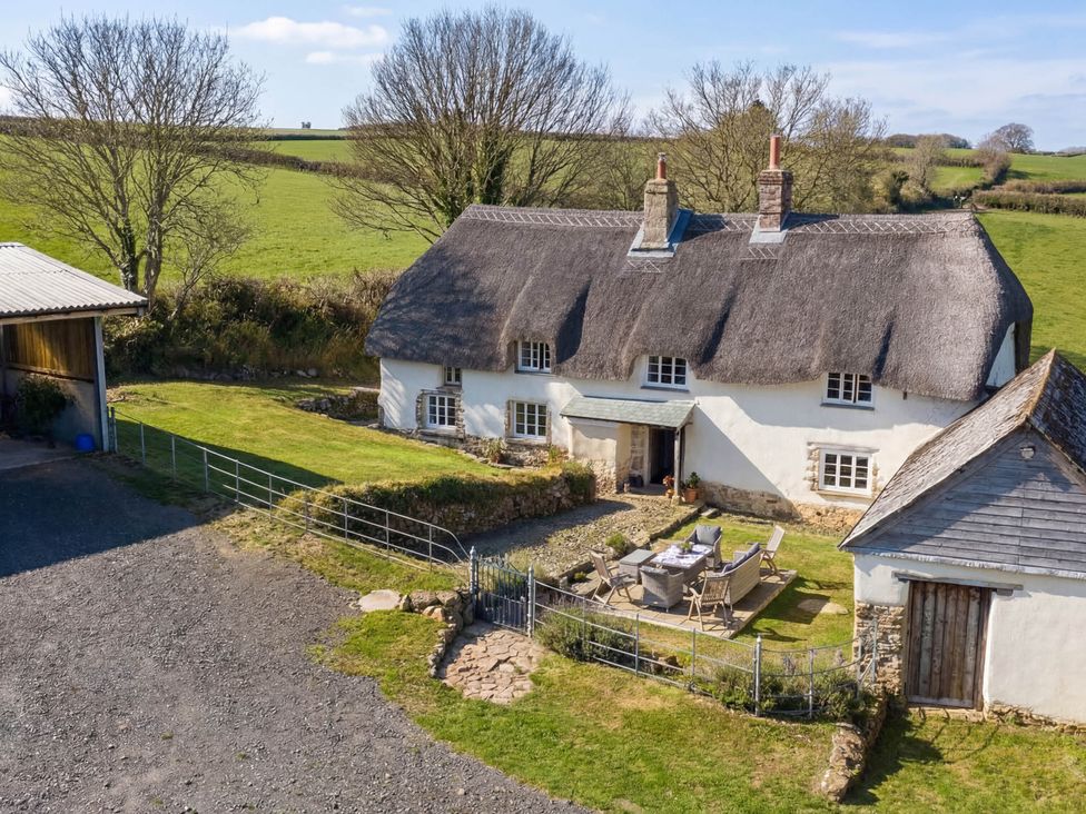An outdoor area with a thatched roof house and patio furniture at Westacombe Farmhouse in Dunsford