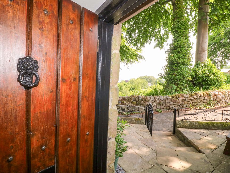 A wooden door with a lion handle and stone steps at Chimney Cottage in Winster