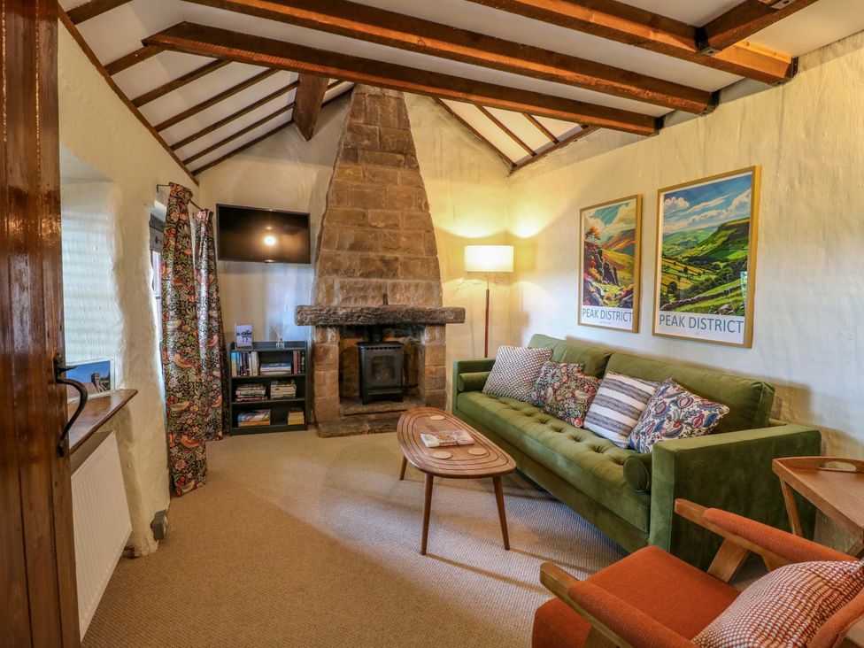 A living room with a green sofa and a fireplace at Chimney Cottage in Winster