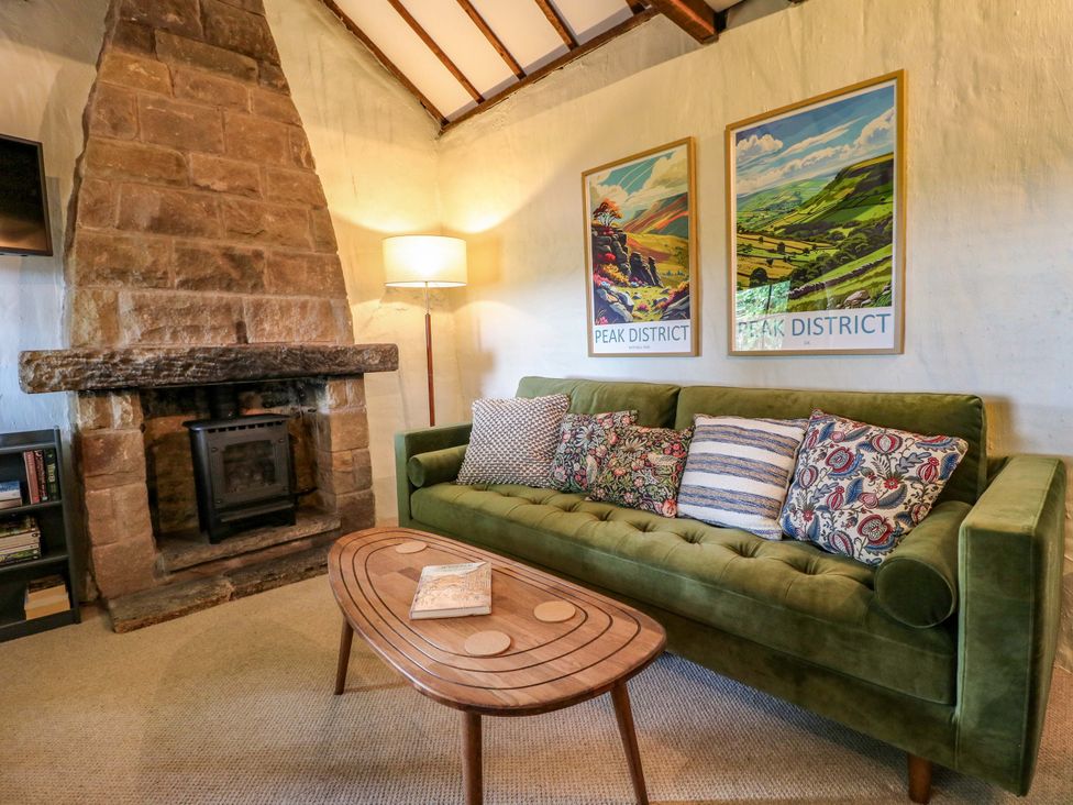 A living room with a green sofa and stone fireplace at Chimney Cottage in Winster