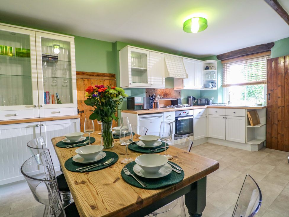 A kitchen with a dining table set and flowers in a vase at Chimney Cottage in Winster