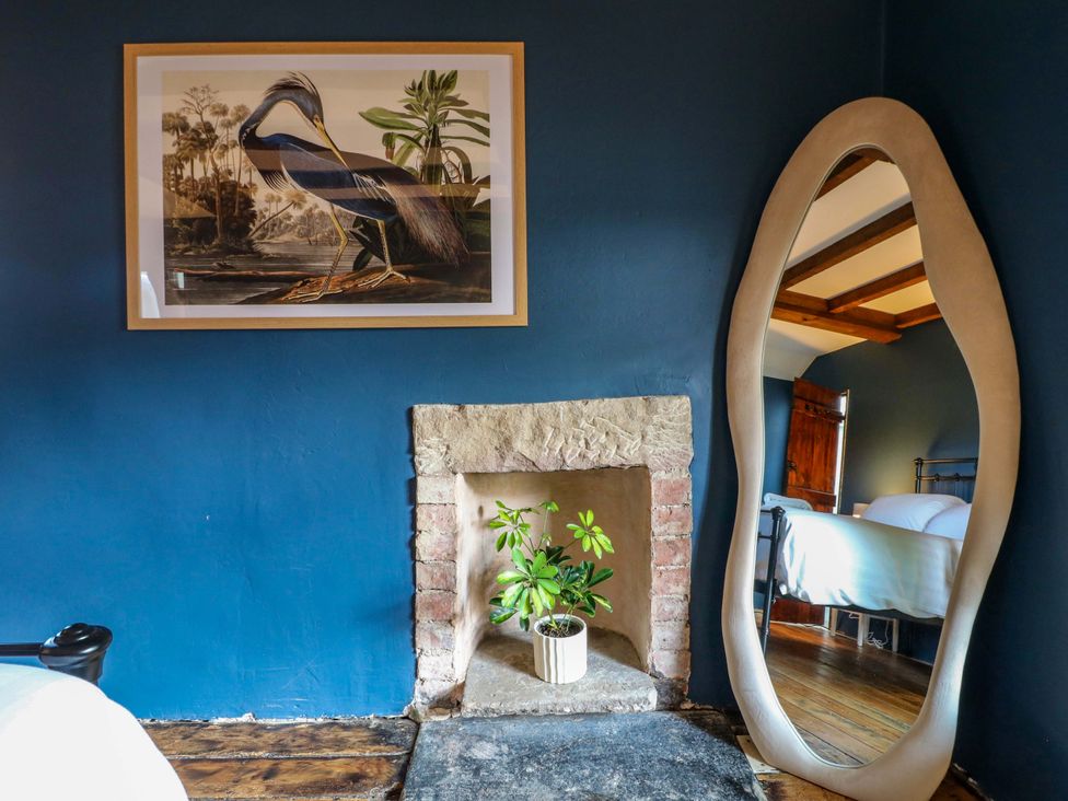 A bedroom with a plant in a fireplace and a large mirror at Chimney Cottage in Winster