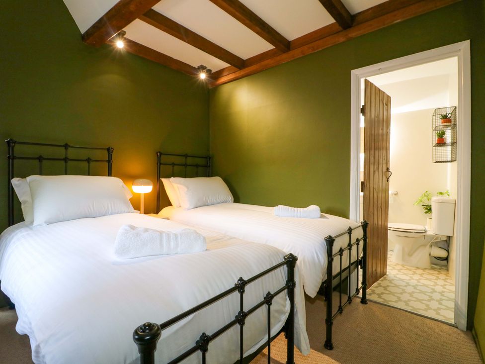 A bedroom with two beds and a door leading to a bathroom at Chimney Cottage in Winster