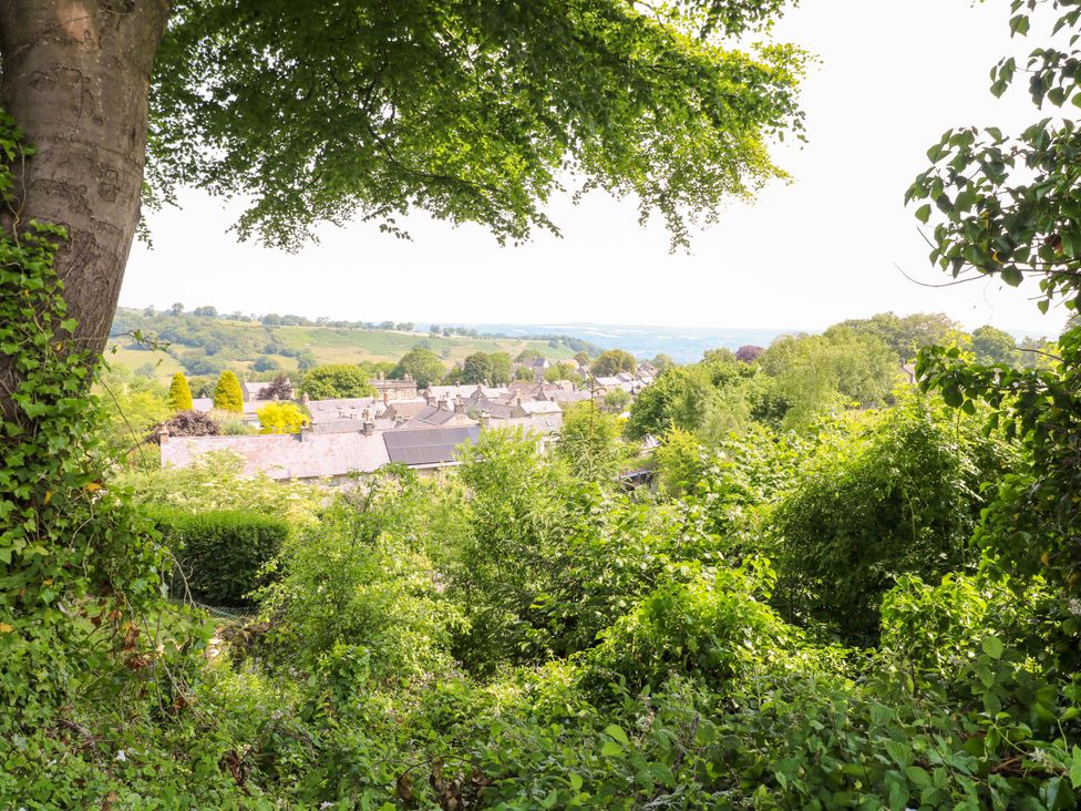 A view of rooftops and hills through trees at Chimney Cottage in Winster