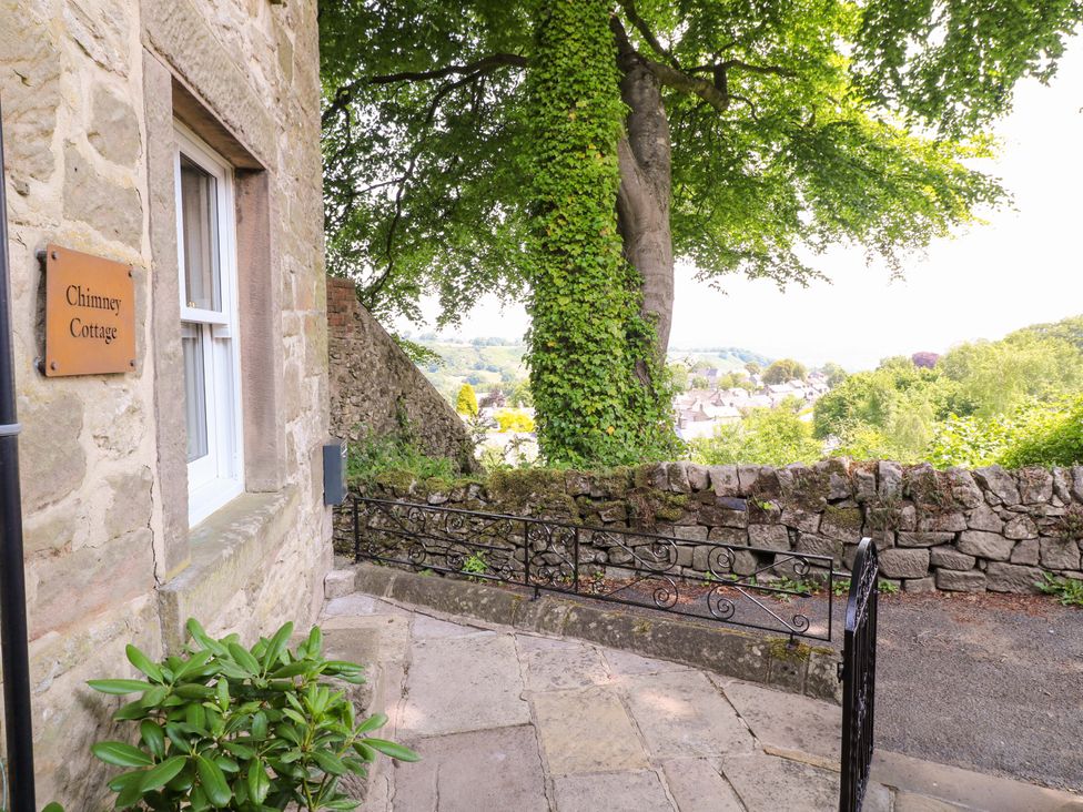 An outdoor view of Chimney Cottage with a stone wall and a tree in Winster