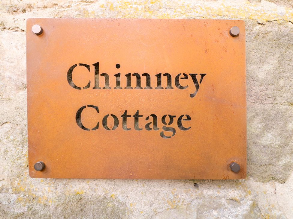 A sign for Chimney Cottage on a stone wall in Winster