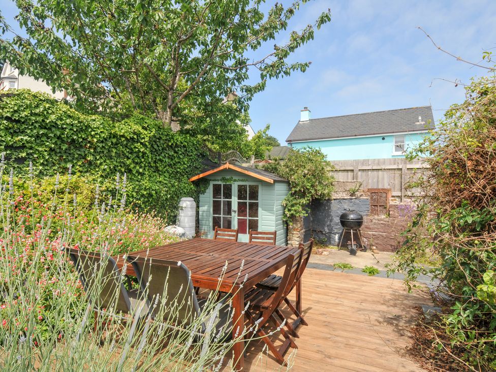 A garden with a wooden table, chairs, shed, and grill at 12 Alpha Place Appledore