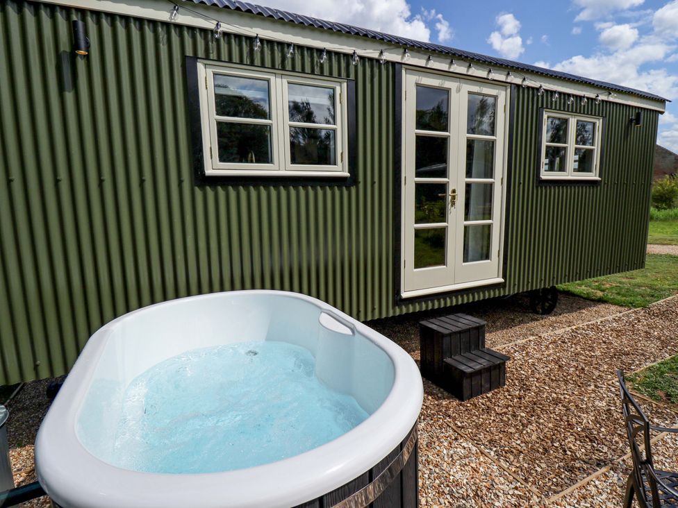 A hot tub beside a green cabin with windows and a door at Primrose in Grimsby