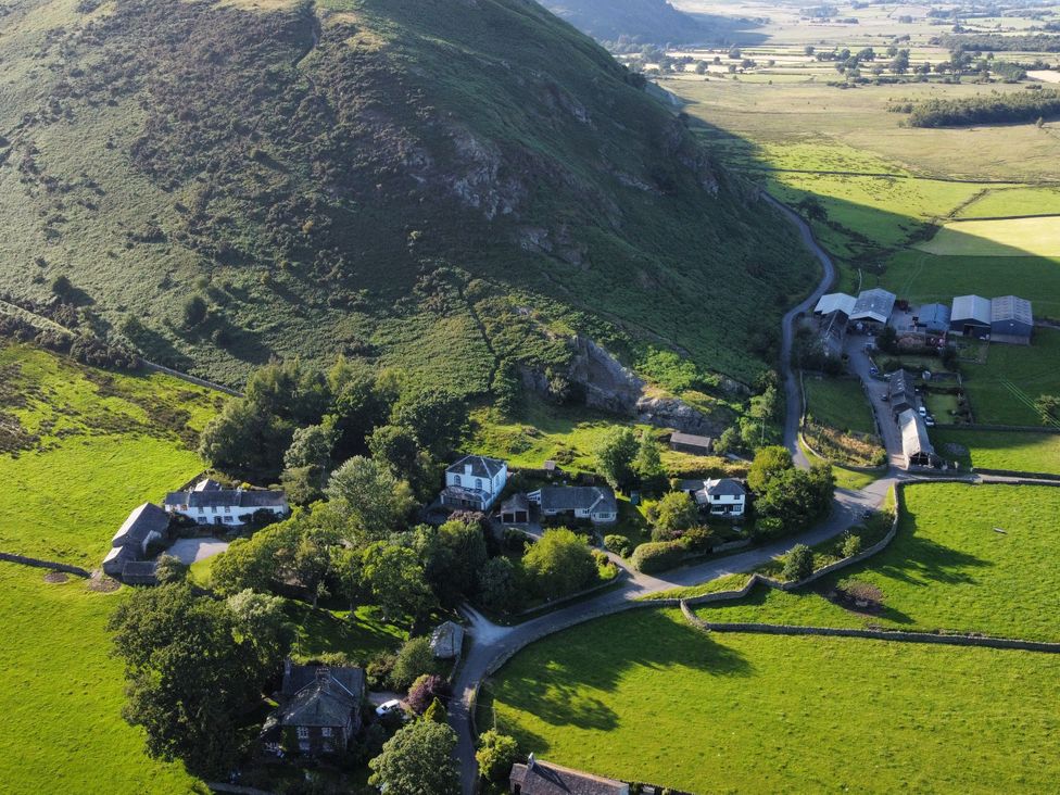 An aerial view of buildings and fields with a hill in the background at The School at Mungrisdale in Mungrisdale near Keswick