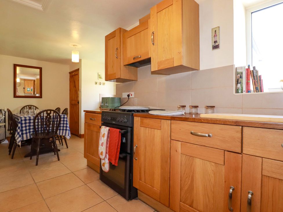 A kitchen with wooden cabinets and a dining area at Brockstone Cottage St Austell