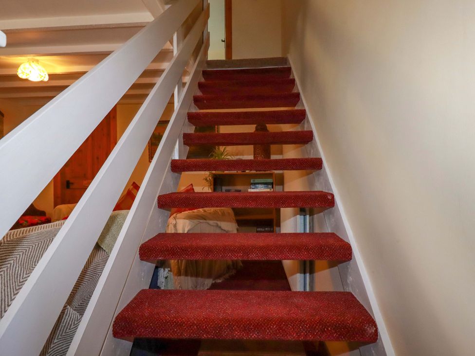 A staircase with red carpet and a handrail at Brockstone Cottage in St Austell