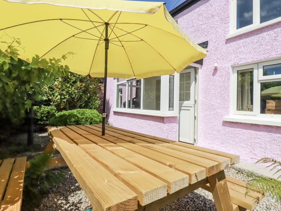 A garden area with a wooden table and yellow umbrella at Brockstone Cottage in St Austell