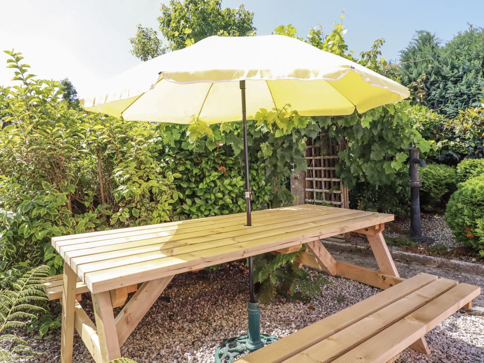 A table with a yellow umbrella in a garden at Brockstone Cottage St Austell