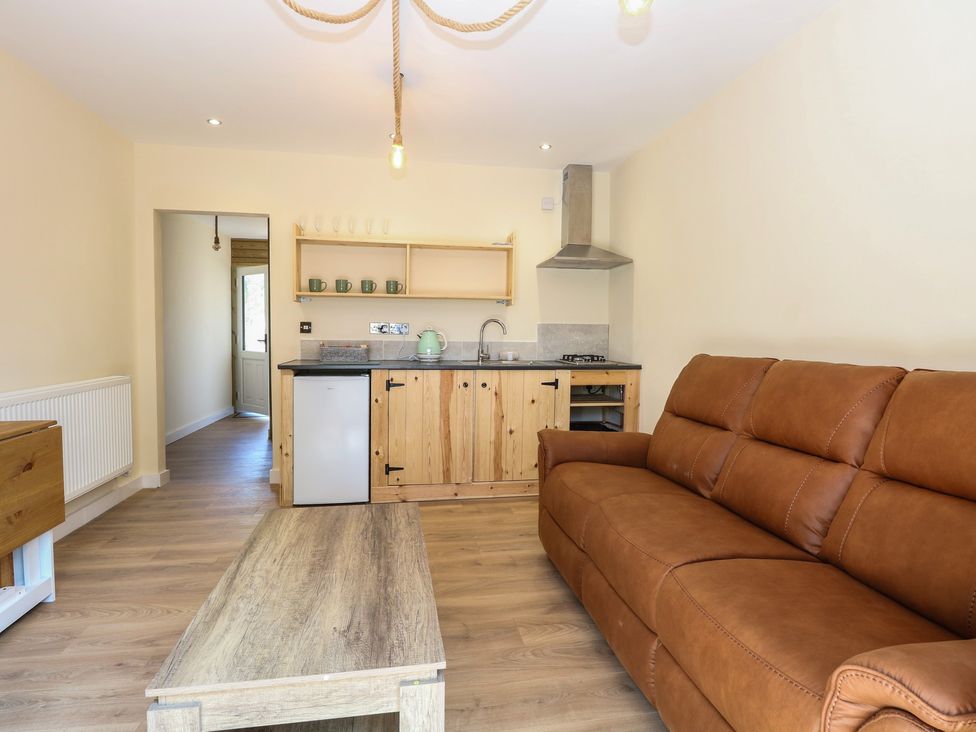 A living room with a sofa, table and kitchen area at Barn Owl Lodge