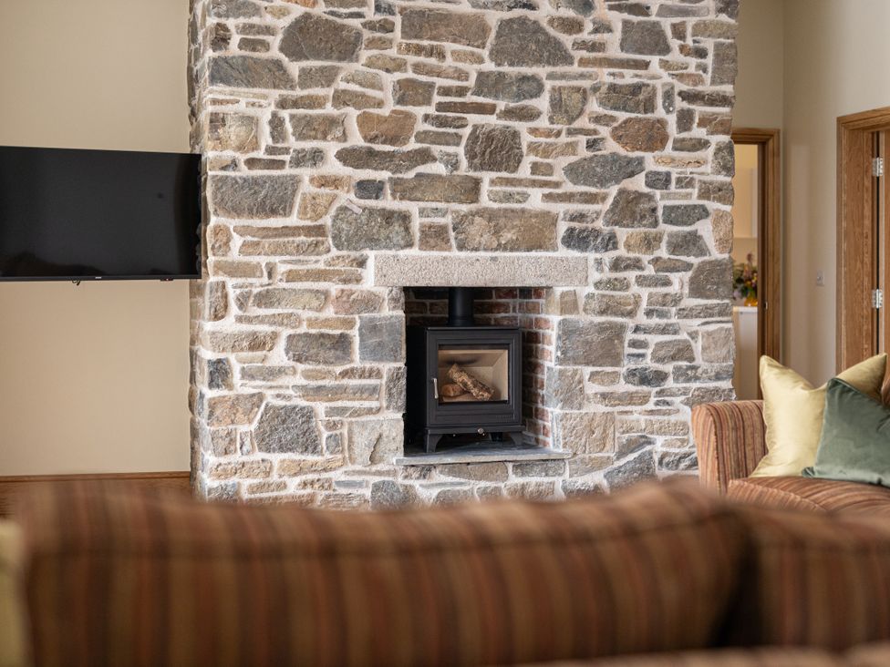 A living room featuring a stone wall and a wood burning stove at Trevean in Mullion