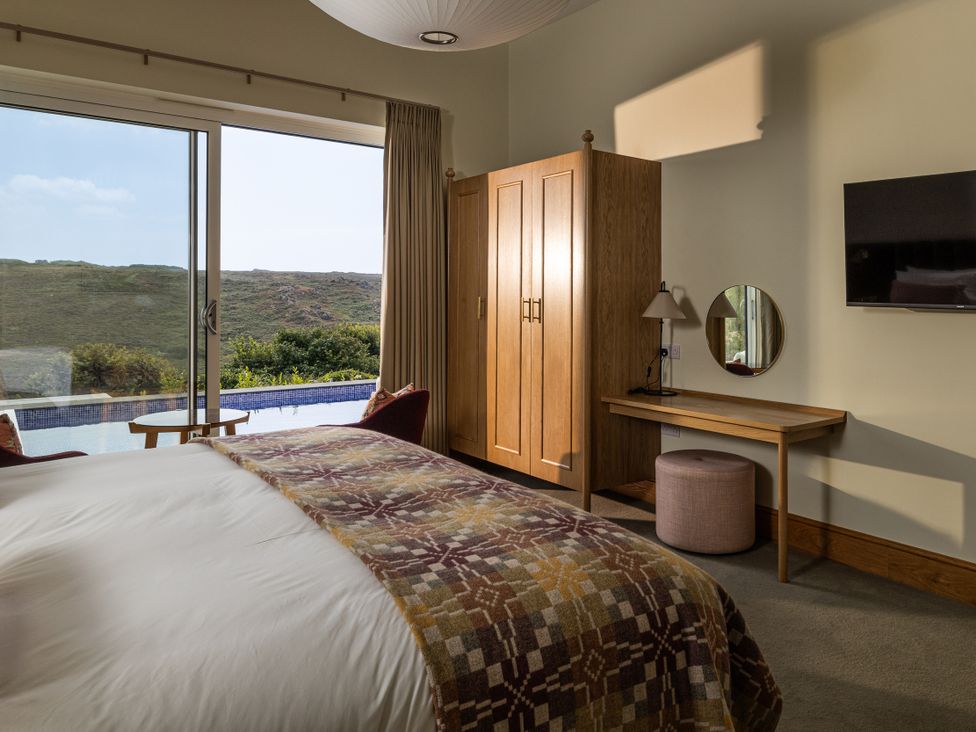 A bedroom with a bed, wardrobe, and desk at Trevean in Mullion