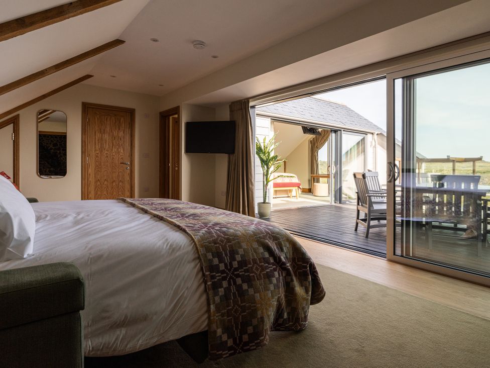 A bedroom with a bed and doors leading to a deck at Trevean in Mullion