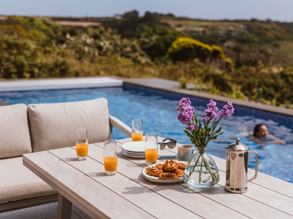 An outdoor table with drinks and snacks by a swimming pool at Trevean in Mullion