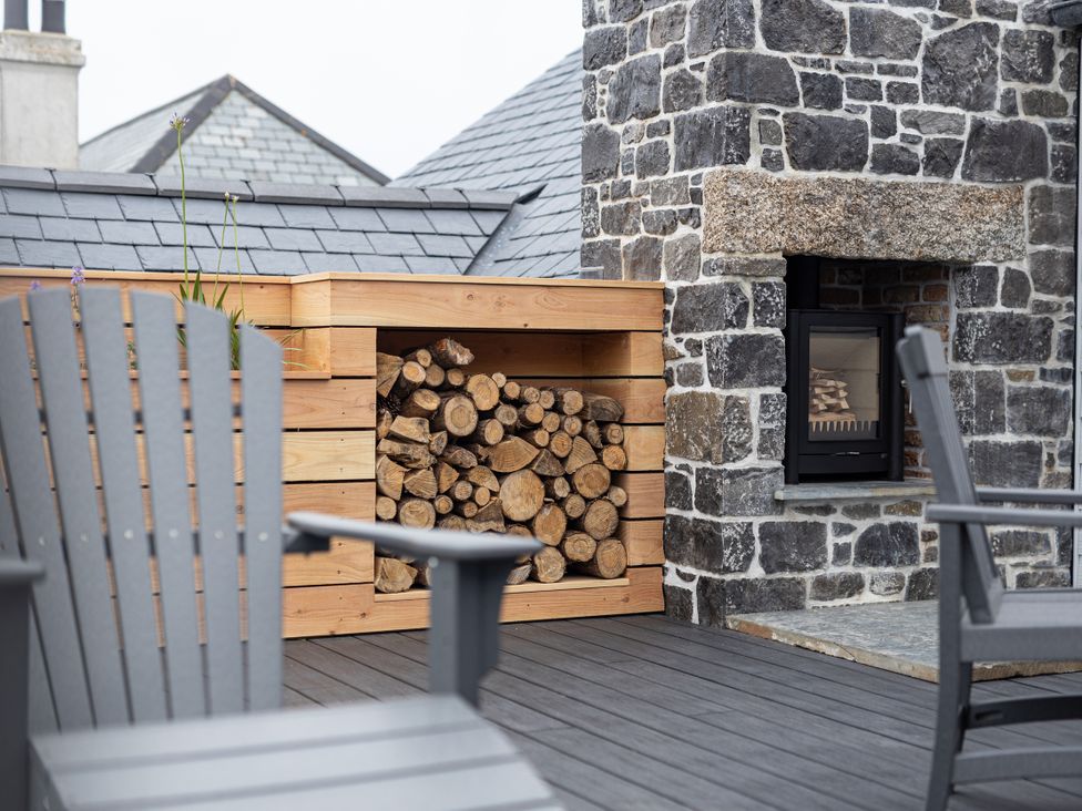 An outdoor area with stacked logs and a stone fireplace at Trevean in Mullion