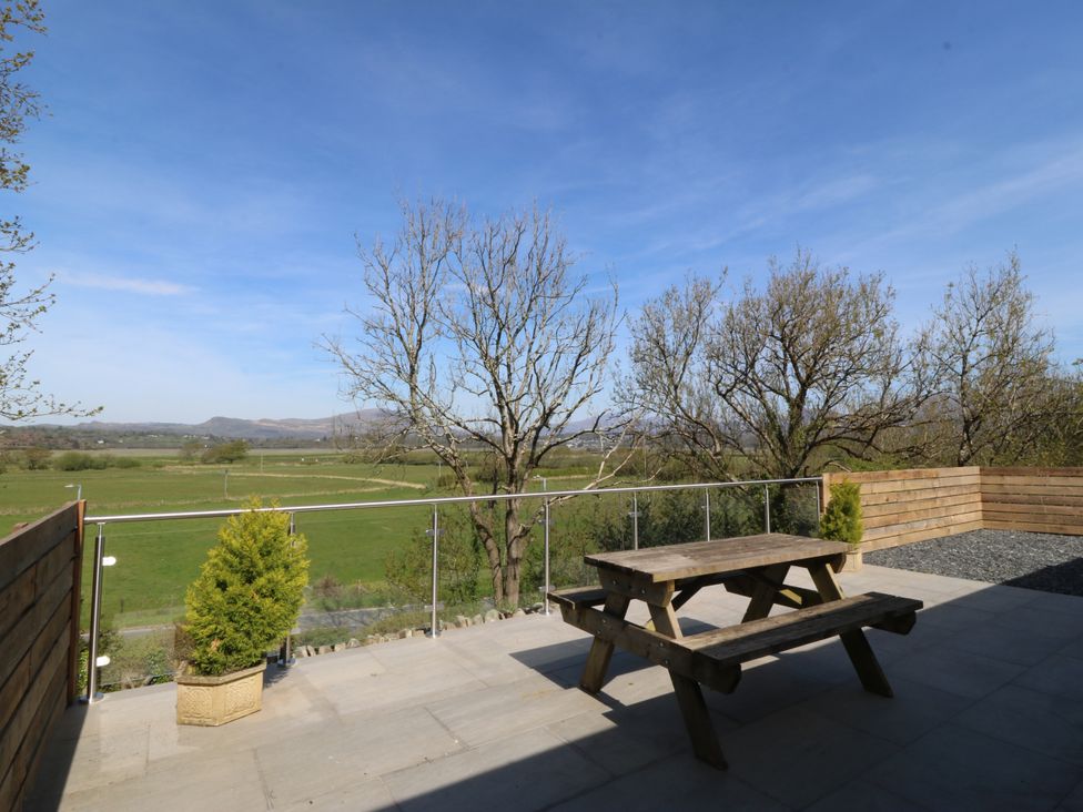 An outdoor area with a wooden table and benches overlooking fields at Tirionfa in Talsarnau