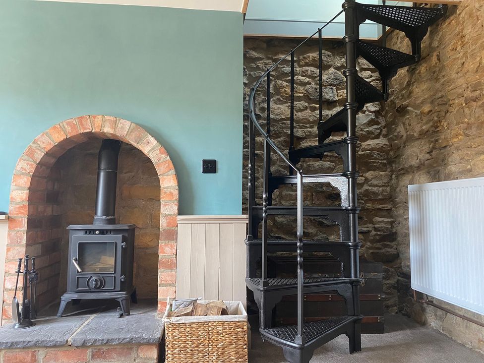 A living room with a wood stove and a spiral staircase at Top Holme Cottage in Newbald